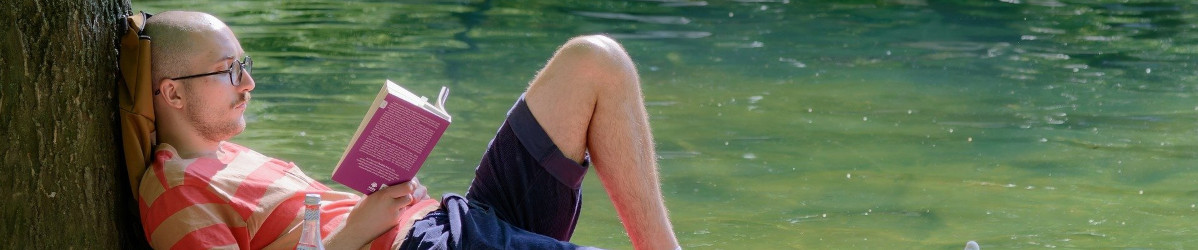 Homme lisant adossé à un arbre au bord de l'eau